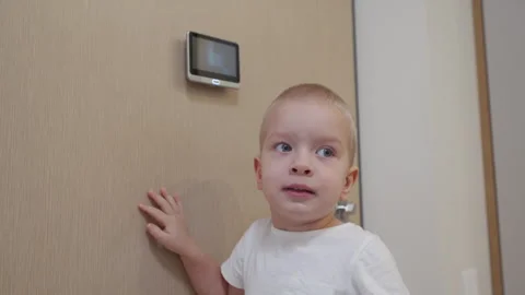 Little boy looking through intercom screen of door peephole surveillance camera Stock Footage 264515525