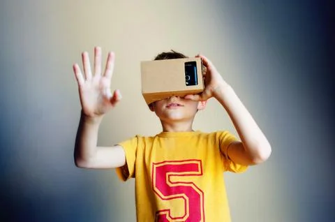 Little boy looking in a VR goggles and gesturing with his hands on gray Stock Photos