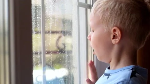 Little boy looking at the window covered with drops of rain 動画素材 89467425
