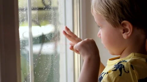 Little boy looking at the window covered with drops of rain 動画素材 89467577