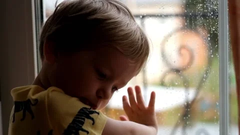 Little boy looking at the window covered with drops of rain Stock Footage 89467700