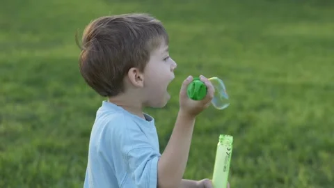 Little boy looks focused while blowing soap bubbles outside. He enjoys the game Stock Footage 317319430
