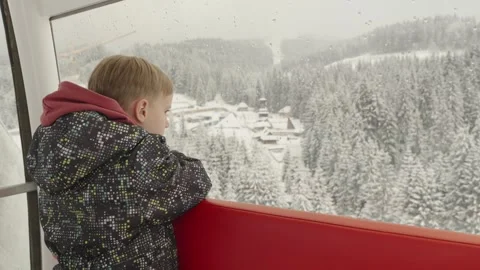 A little boy looks at the mountain landscape from the cab of a Ferris wheel Stock Footage 295800053