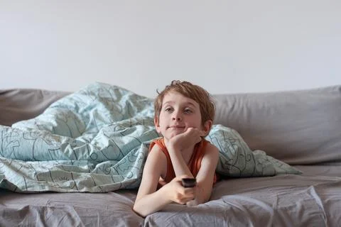 Little boy lying on a bed with remote control. Stock Photos