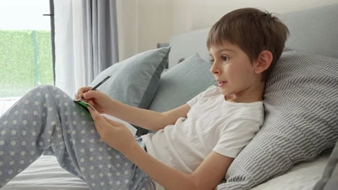 Little boy lying in bed, writing in notebook and ding homework. Concept of educa Stock Footage 239123167