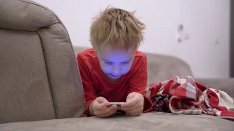 Little boy is lying on couch with smartphone in hands and playing mobile game or Stock Footage 146690913