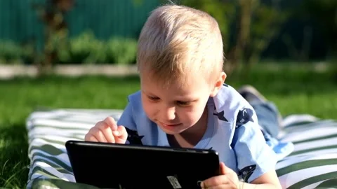 Little boy lying on grass and playing with Tablet, summer outdoors Vídeos de archivo 89517481