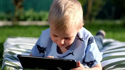 Little boy lying on grass and playing with Tablet, summer outdoors Vídeo Stock 89517810