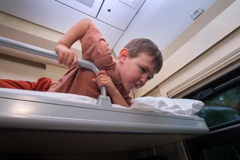 Little boy lying on upper bunk in train compartment looking down. Child trave Stock Photos