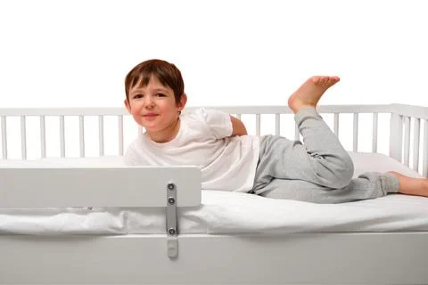 Little boy lying on white bed with safety rail isolated on white background.. Stock Photos