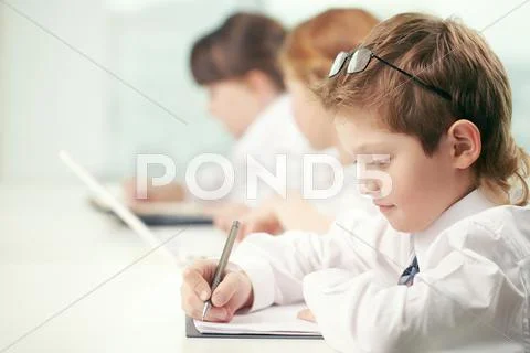 Little boy making classwork with other pupils Stock Photos