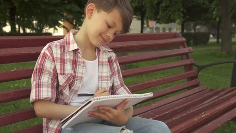 Little boy notes in exercise book on the bench Stock Footage 79618155