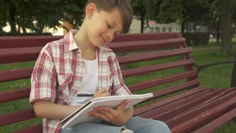 Little boy notes in exercise book on the bench Stock Photos
