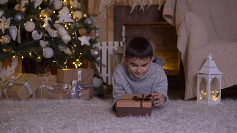 A little boy opens a box with a gift and rejoices lying on the floor near the Stock Footage 98818454