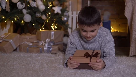 A little boy opens a box with a gift and rejoices lying on the floor near the Stock Footage 98818581