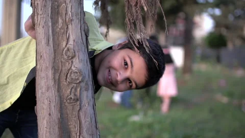 Little boy overlooking from behind a tree trunk, slow motion Stock Footage 133380315