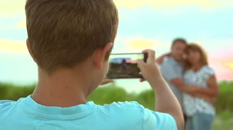 Little boy photographing with smart phone his parents outdoors. Stock Footage 67355953