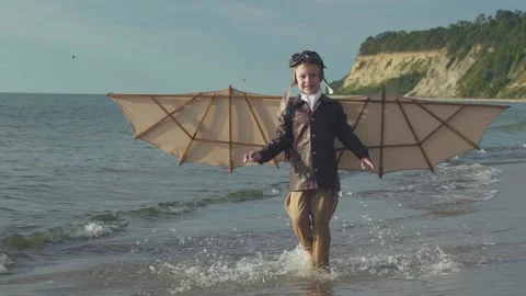 Little boy in pilot suit with artificial wings on his back runs along seashore. Stock Footage 279898142