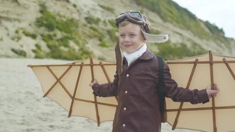 Little boy in pilot suit with artificial wings on his back walks along seashore. Stock Footage 279898501