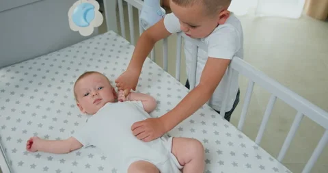 Little boy playing and holding the hand of his newborn brother who is lying in Stock Footage 219345760