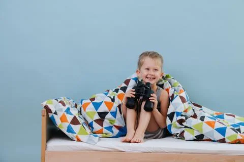 Little boy is playing in bed holding binoculars in hands over blue walls Stock Photos