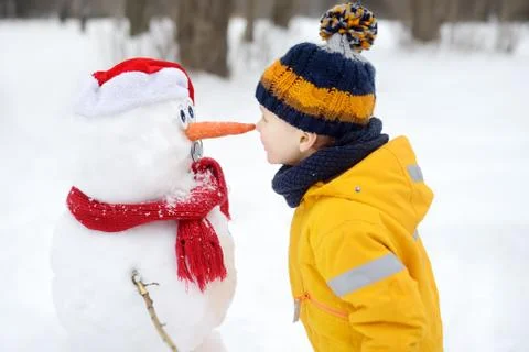 Little boy playing with funny snowman. Child reaches for a snowman's carrot n Stock Photos