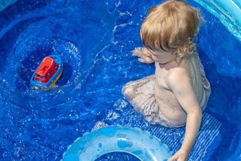 A little boy is playing in the inflatable pool in the summer garden 스톡 사진