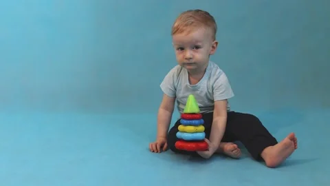 Little boy playing with a multi-colored pyramid sitting on a blue background Stock Footage 169627054