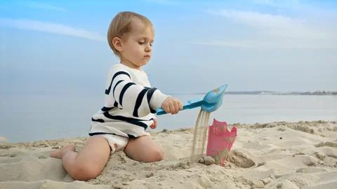 Little boy playing on the sandy beach with toys and using a shovel to dig s.. Stock-Fotos