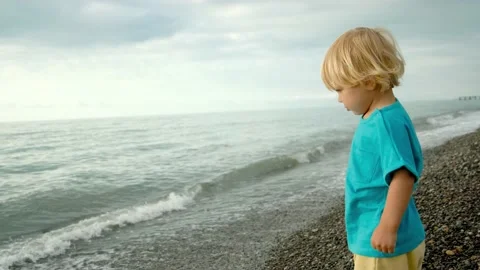 A little boy is playing on the seashore, he throws stones into the water. Family Stock Footage 200807566