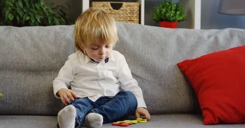 Little boy playing with three spinners while sitting on the grey couch with red Stock Footage 82917504