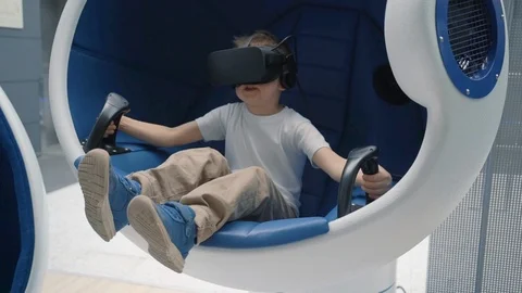 Little boy playing virtual reality in a moving interactive chair Stock Footage 106750064