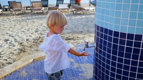 Little boy playing with water in a tap on the beach Stock Footage 200784552