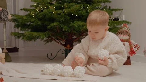 Little boy plays with baubles while decorating the Christmas tree in a cozy room Stock Footage 346697418