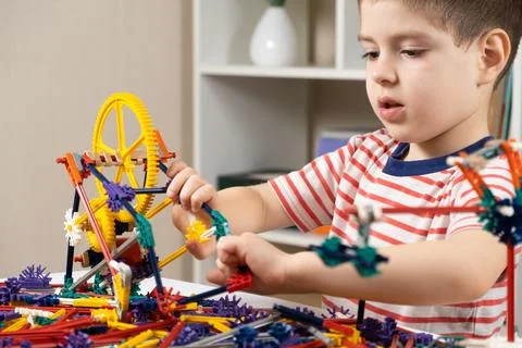 A little boy plays with a constructor, creating figures from gears and sticks Stock Photos