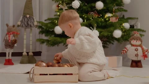 Little boy plays with decorations next to a Christmas tree in living room Stock Footage 346698018
