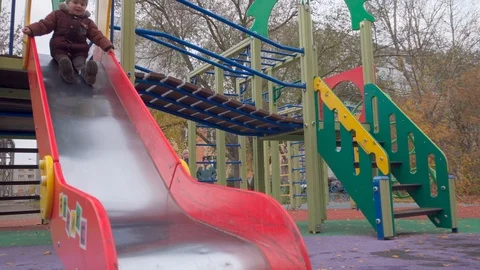 Little boy plays on the playground, slides down the slide runs for another ride Stock Footage