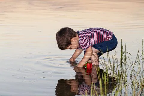 A little boy plays on the river bank, the reflection of a child in the water. Stock Photos