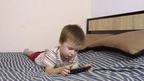 Little boy plays in a smartphone while lying on a big bed. Stock Footage 141497045