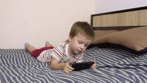 Little boy plays in a smartphone while lying on a big bed. Stock Footage 141620526