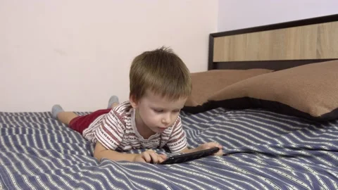 Little boy plays in a smartphone while lying on a big bed. Stock-Footage 141684606