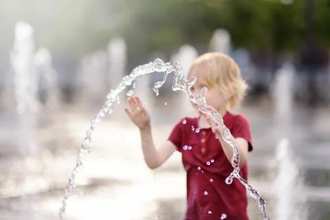 Little boy plays in the square between the water jets in the fountain at sunn Foto stock