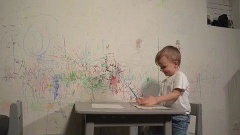 A little boy plays at the table in front of the wall he painted at home. Stock Footage 230929461