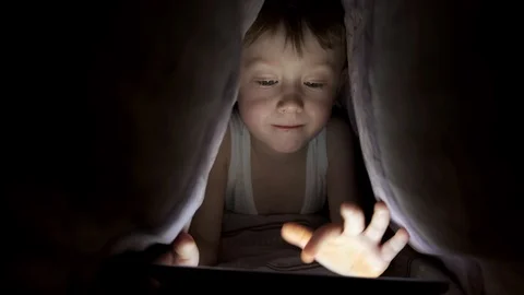 Little boy plays on tablet while lying under blanket. watching cartoons hiding Stock-Footage 125927201
