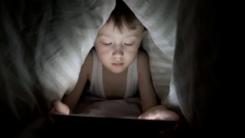 Little boy plays on tablet while lying under blanket. watching cartoons hiding Stock-Footage 125927204