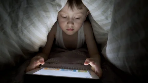 Little boy plays on tablet while lying under blanket. watching cartoons hiding Stock-Footage 125927215