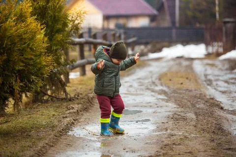 Little boy in protective rubber boots and rain clothes jumping in mud puddle Foto stock