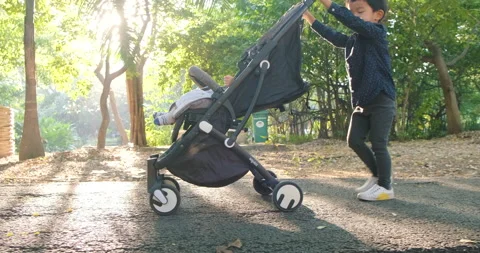 Little boy push baby stroller recreation in tree park Stock Footage 166507875