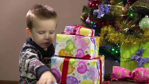 A little boy puts gift boxes in a pyramid under the tree.He is pleased with his 库存影片 162563383