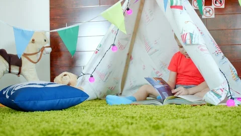 Little boy is reading book in his self made wigwam in playroom Stock Footage 87845913